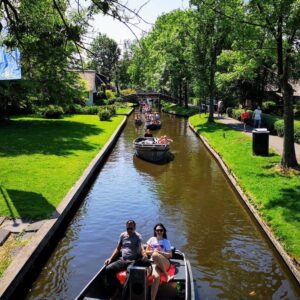 Main canal of Giethoorn with electric sloops on the water and a scenic walking path beside traditional Dutch houses.